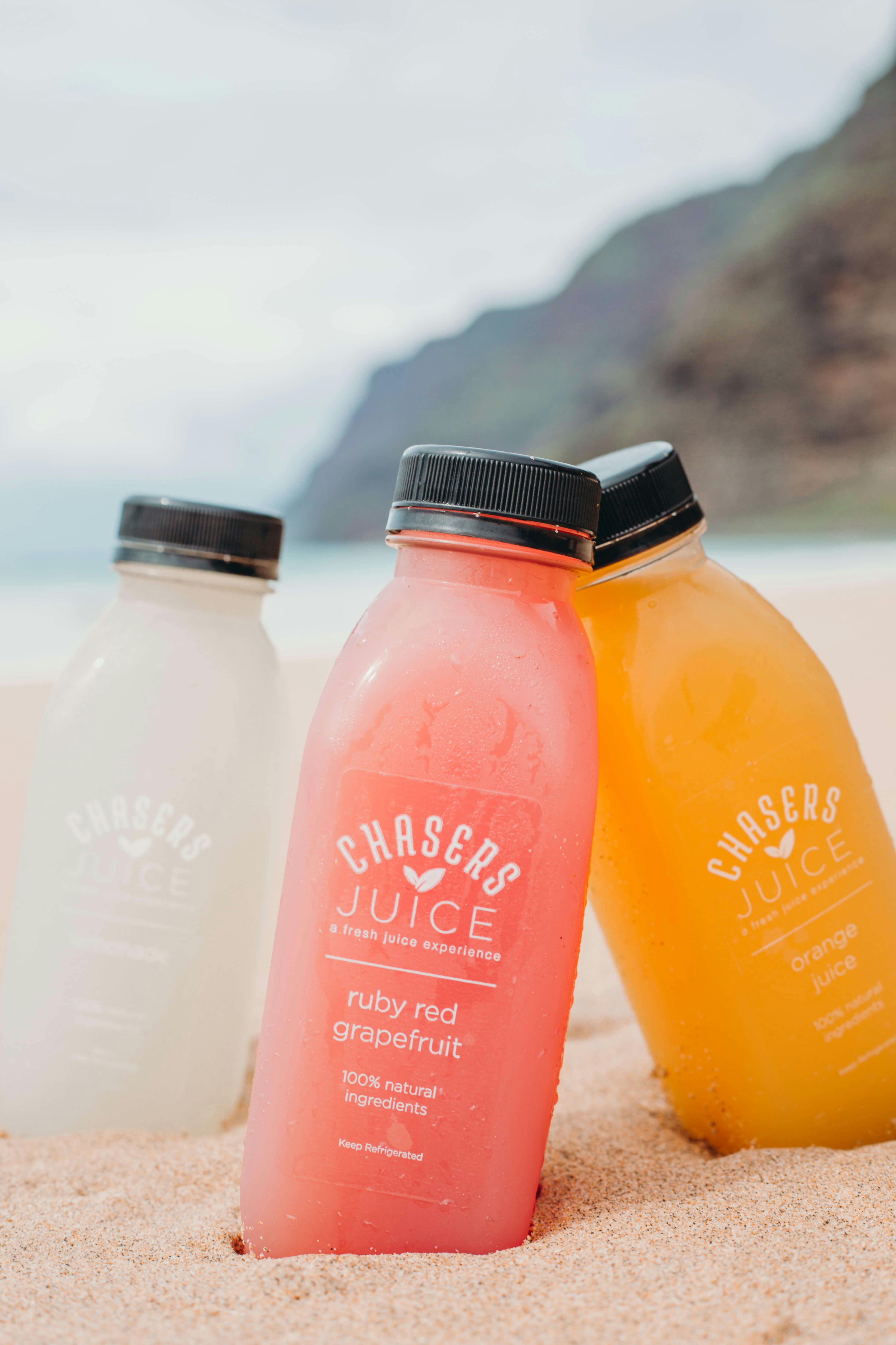 Three bottles of different juices on a beach